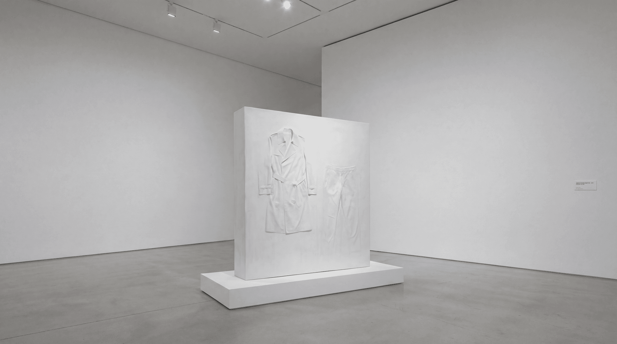 Visiteur face au panneau monumental en plâtre blanc avec relief d’un trench Margiela